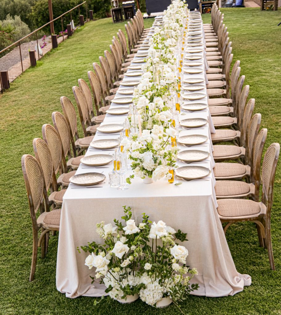 Lang gedeckter Hochzeitstisch mit weißer Blumendeko, Gläsern und Kerzen – Sommerhochzeit auf Mallorca im Freien

